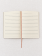 An open lined notebook with cream-colored pages and a thin rose gold ribbon bookmark, displayed flat against a light gray background.