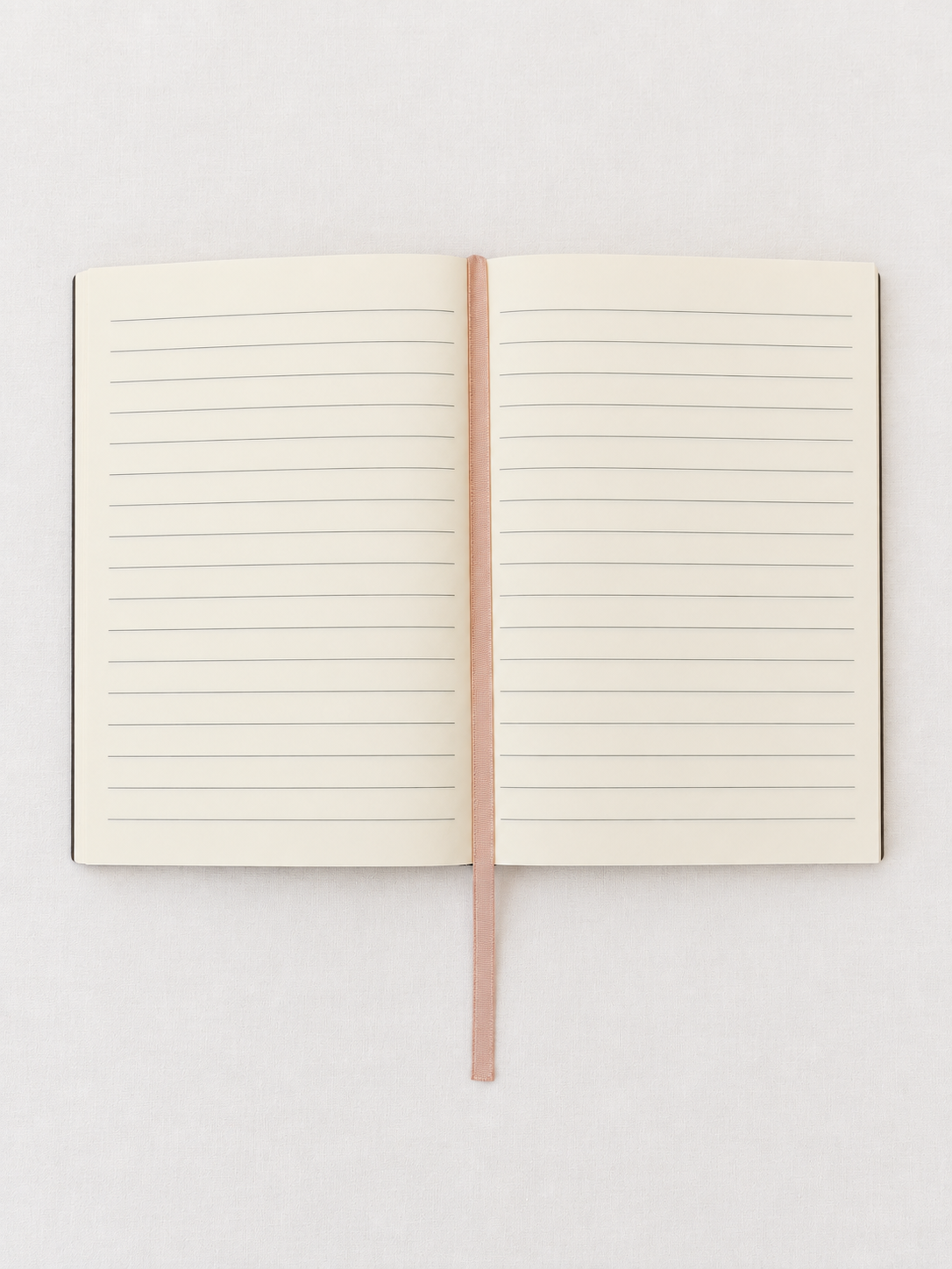 An open lined notebook with cream-colored pages and a thin rose gold ribbon bookmark, displayed flat against a light gray background.