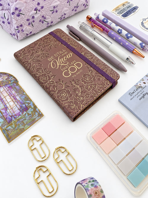 Close-up of Be Still gold embossed Scripture journal with coordinated purple pens and page tabs